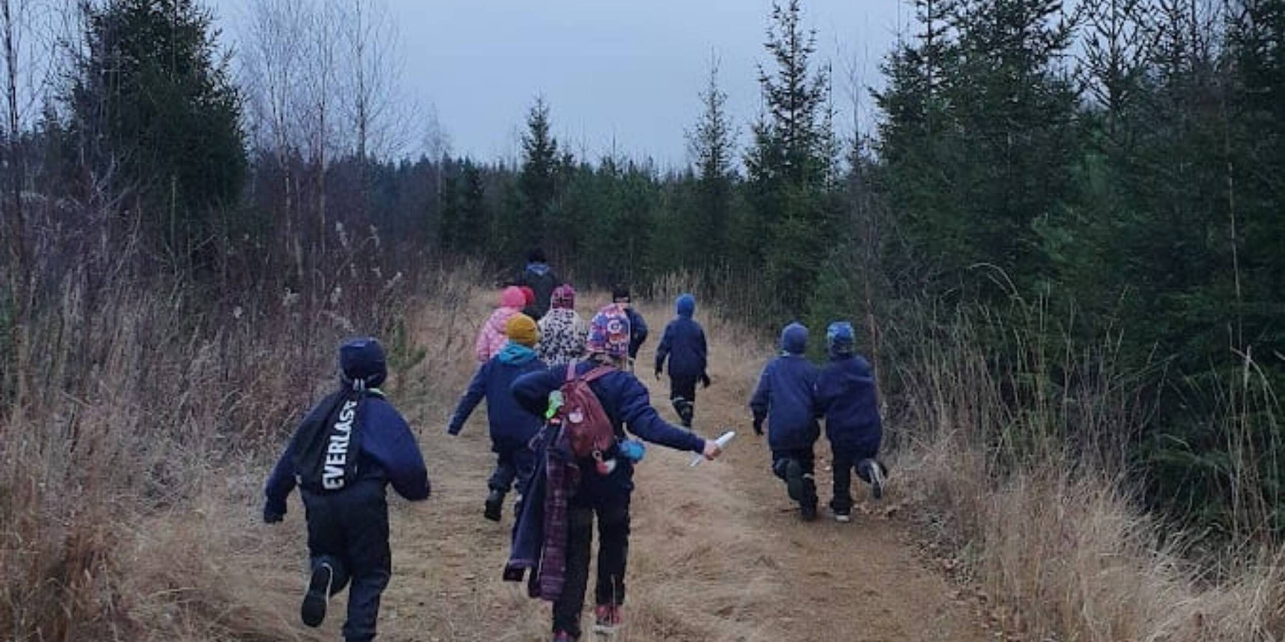 Nuoria partiolaisia juoksemassa metsätiellä.